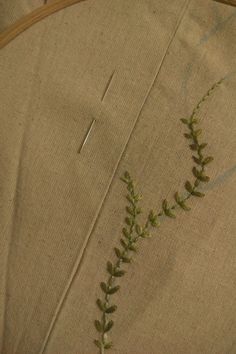 a close up of a piece of cloth with green plants on it and thread in the middle