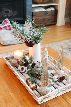 a tray with candles, pine cones and evergreen branches in it on a coffee table