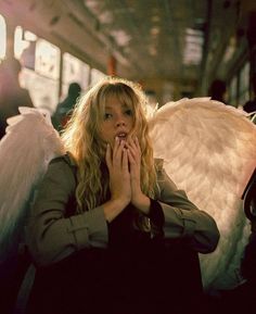 a woman sitting on a bus with an angel wings in her lap and hands clasped to her chest