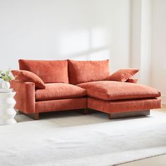 an orange couch with pillows on it in front of a white rug and vases