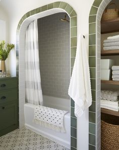 a bathroom with green tile and white towels on the shelf next to the bathtub