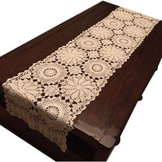 a table runner with crocheted doily is on a wooden surface and sits on top of a dark wood cabinet