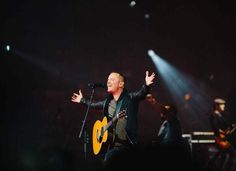 a man singing into a microphone while holding a guitar in front of him on stage