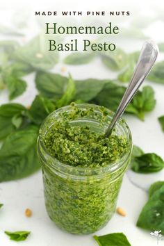 homemade basil pest in a glass jar with a spoon on the side and green leaves surrounding it