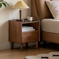 a nightstand with a lamp on top of it next to a bed