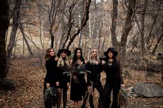 four women dressed in black posing for the camera with their hats on and flowers in their hands