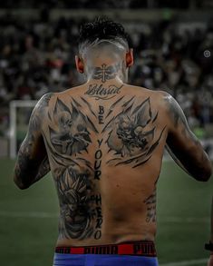 a man with tattoos on his back standing in front of a soccer field