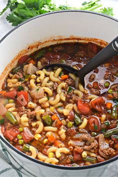 a large pot filled with pasta and meat soup on top of a table next to a spoon