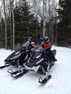 two people on snowmobiles in the woods