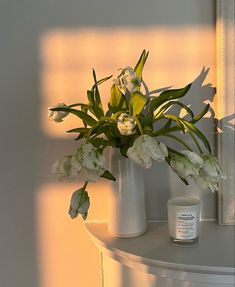 a white vase filled with flowers sitting on top of a table next to a candle