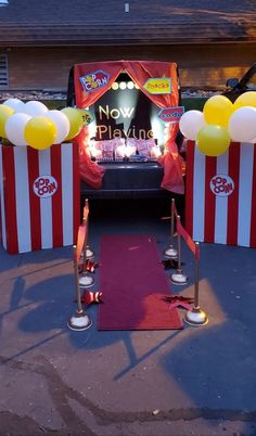 a red carpeted area with white and yellow striped barriers, balloons and stage set up for a circus themed event