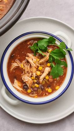 a bowl of chicken tortilla soup with cilantro and corn on the side