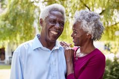 an older man and woman smile as they stand in front of a tree, with their arms around each other