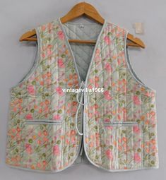 a vest with flowers on it hanging on a hanger in front of a white wall