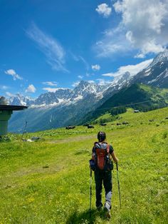 a man hiking up a grassy hill with mountains in the background