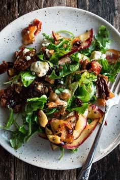 a white plate topped with salad next to a fork and knife on top of a wooden table