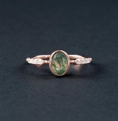 a gold ring with a green tourmaline and white diamonds on the side, sitting on a black surface