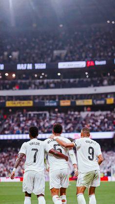 three soccer players huddle together on the field in front of an empty stadium full of people