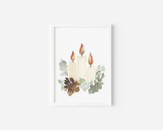 two lit candles with leaves and acorns on a white background in a frame