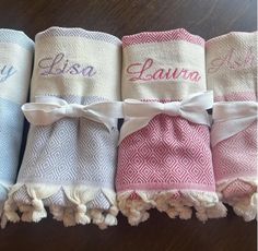 four personalized towels are lined up on a wooden table with tassels and bows