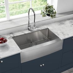 a stainless steel kitchen sink with marble counter tops and blue cabinets in front of a window