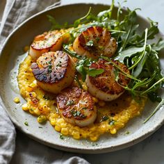 a white plate topped with scallops and corn on top of a bed of greens