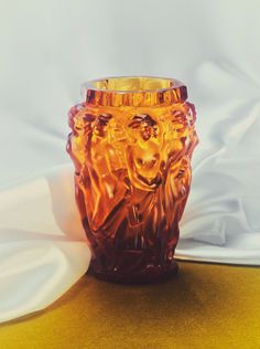 an orange glass vase sitting on top of a yellow tablecloth covered floor next to a white sheet