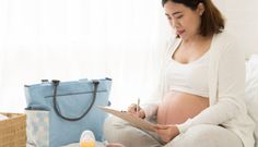 a pregnant woman sitting on her bed reading a book