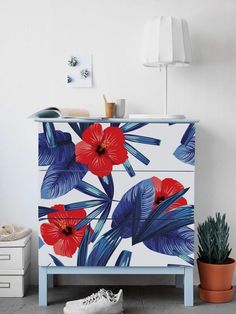 a white dresser with red and blue flowers painted on the drawers next to a potted plant