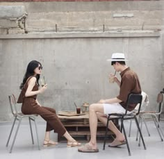 a man and woman sitting at a table with drinks in their hands while talking to each other