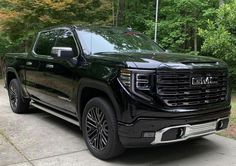 a black truck is parked on the side of the road in front of some trees