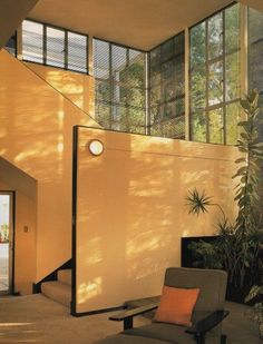 a living room filled with furniture next to a tall window covered in plants and windows