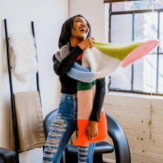 a woman is laughing while holding a multicolored scarf