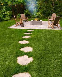 a fire pit in the middle of a grassy area with chairs and lights on it