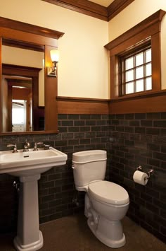 a white toilet sitting next to a sink in a bathroom under a mirror with wooden trim