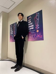 a man in a tuxedo leaning against a wall with posters on the wall behind him