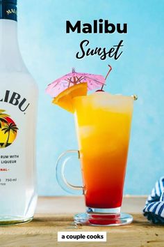 a bottle of malibu sunset next to a glass filled with orange juice and an umbrella