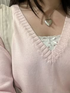 a woman wearing a pink sweater with a heart shaped pendant on her neck and chest