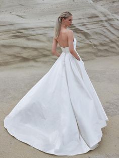 a woman in a white wedding dress standing on the beach with her back to the camera