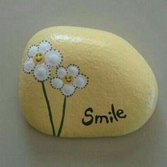 a rock with flowers painted on it and the word smile written in black ink, sitting on a white surface