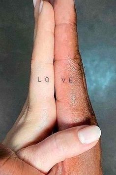 two hands holding each other with the word love tattooed on their thumbnails in front of them