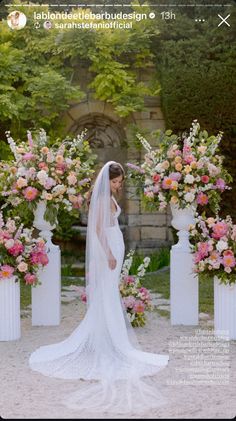 a woman in a wedding dress is standing next to some flowers and pillars with pink and white flowers on them