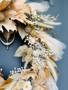 a close up of a wreath on a door with flowers and leaves around it in front of a blue door