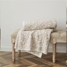 a white and beige blanket sitting on top of a wooden bench next to a wall