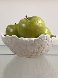 two green apples sitting in a white bowl