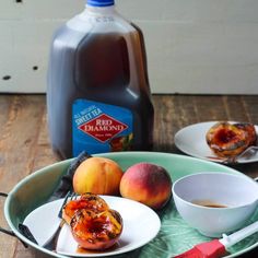 a plate with some peaches on it next to a bottle of syrup and a cup