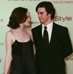 a man and woman standing next to each other in front of a red carpeted wall