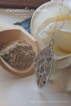 a white rose sitting next to a spoon filled with sand and a silver necklace on a chain