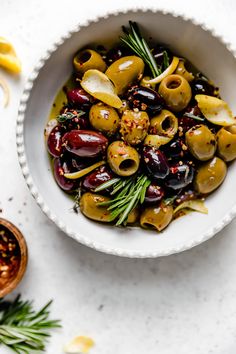 a bowl filled with olives and herbs on top of a white table next to other ingredients