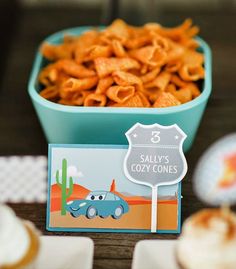 a table topped with cupcakes and cookies next to a bowl filled with macaroni and cheese